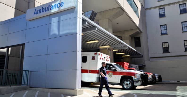 Emergency first responder walks in a hospital parking lot in front of an ambulance.